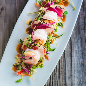 Photo of a Shrimp display and sliced sesame seared tuna on a rectangular plate with baby greens and soy glaze 