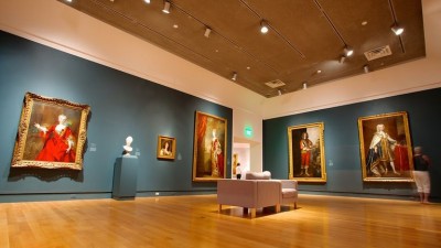 Photo of Gallery room with wood floors, hanging art, blue wall and lounge chairs. 