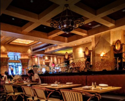 Dining area of Cheesecake factory with dimmed lights and booths/chairs.